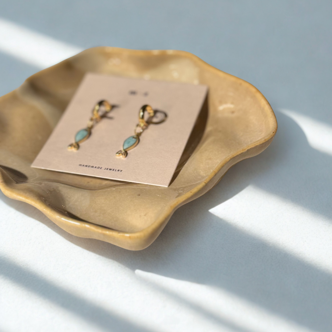 Pair of earrings on a card inside a brown ceramic dish with a light background